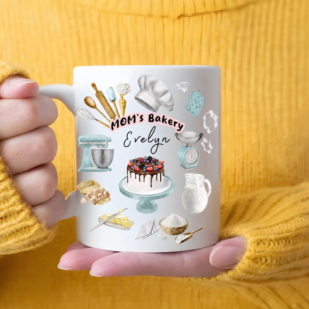 Hands in a yellow sweater cradling a MOM's Bakery custom name mug with berry cake and mint mixer design