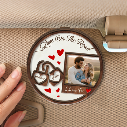 Hand holding a personalized Love On The Road wooden photo clip with two heart locks and couple picture on a visor