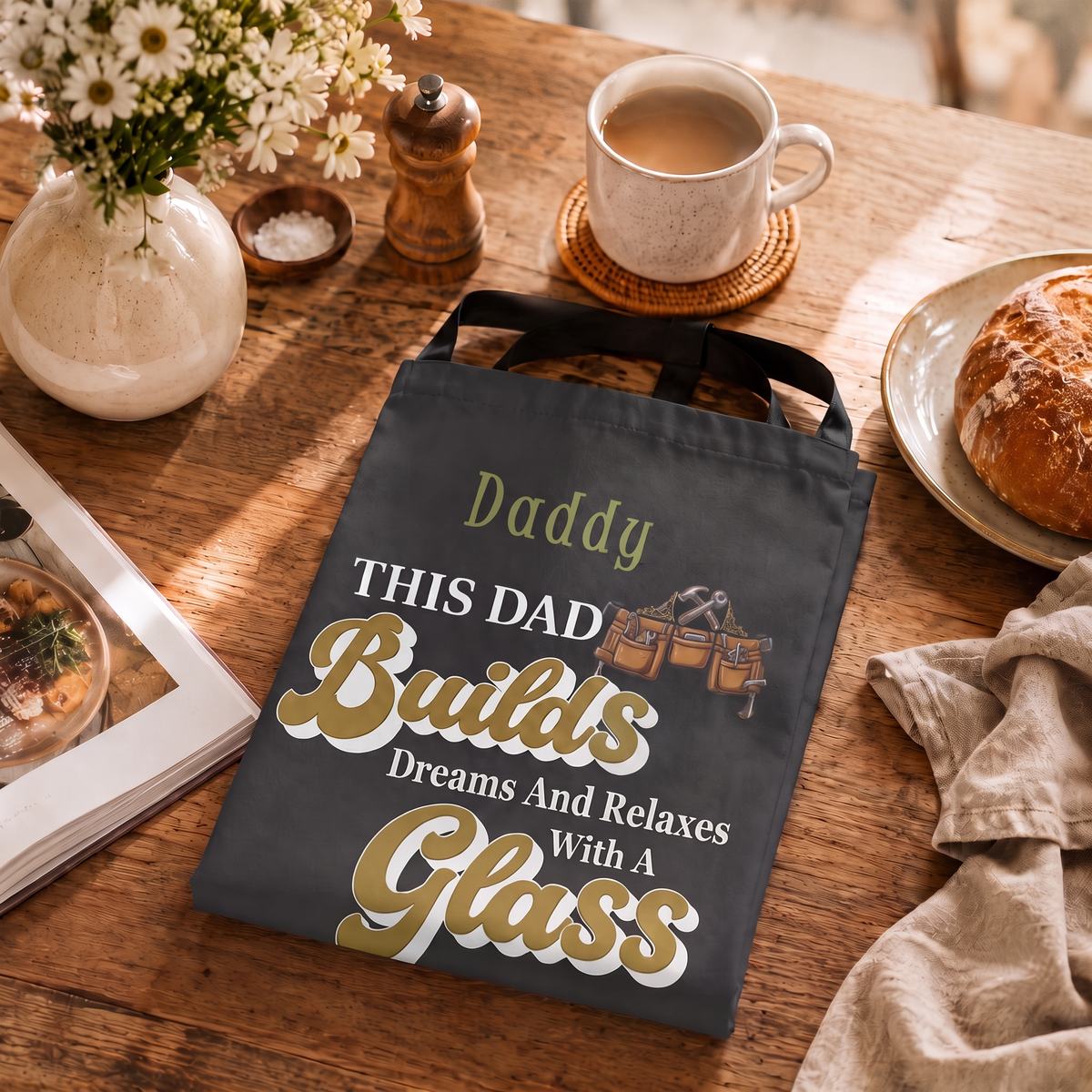Charcoal Daddy This Dad Builds Dreams apron folded on a rustic breakfast table beside coffee and fresh bread