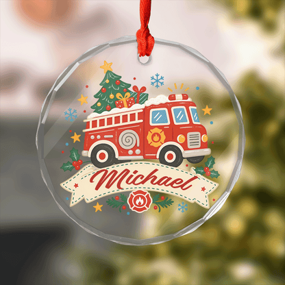 Round clear glass ornament with a fire truck carrying a Christmas tree and gifts and a custom name banner
