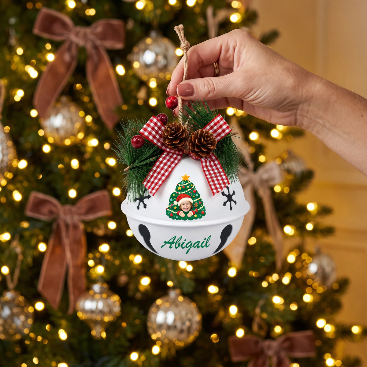 Hand holding a personalized kid photo jingle bell ornament by the Christmas tree