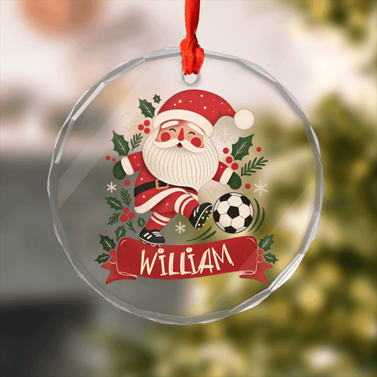 Round clear glass ornament with Santa kicking a soccer ball, holly and a custom name banner