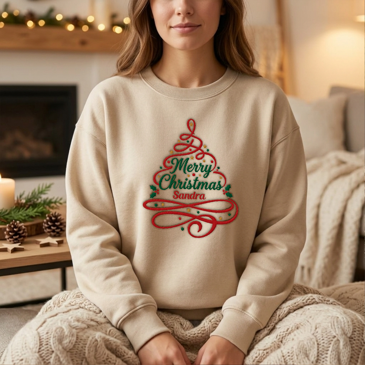 Woman wearing the sand Merry Christmas Ribbon Tree embroidered sweatshirt with custom name by a cozy fireplace